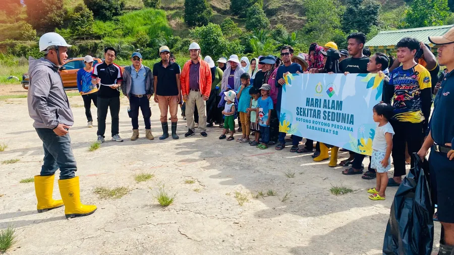 Our team with villagers at Gotong Royong Perdana 2025, holding a World Environment Day banner