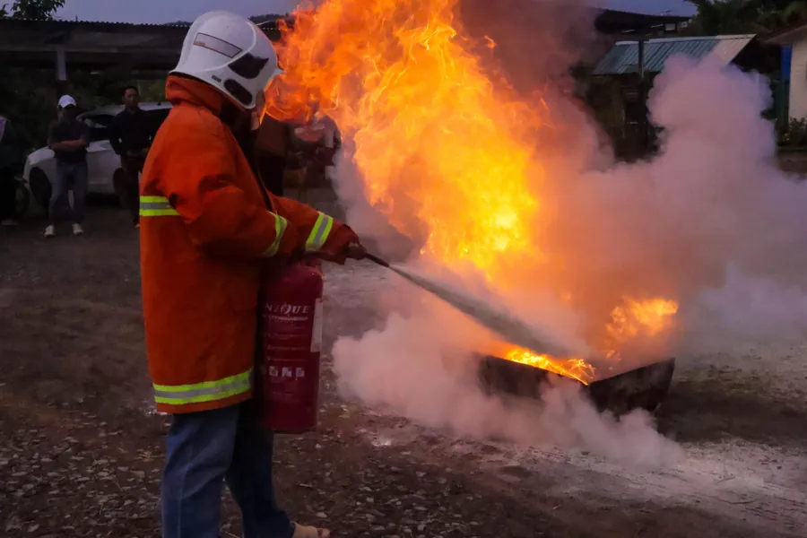 A worker in fire gear puts out a fire with an extinguisher during safety training